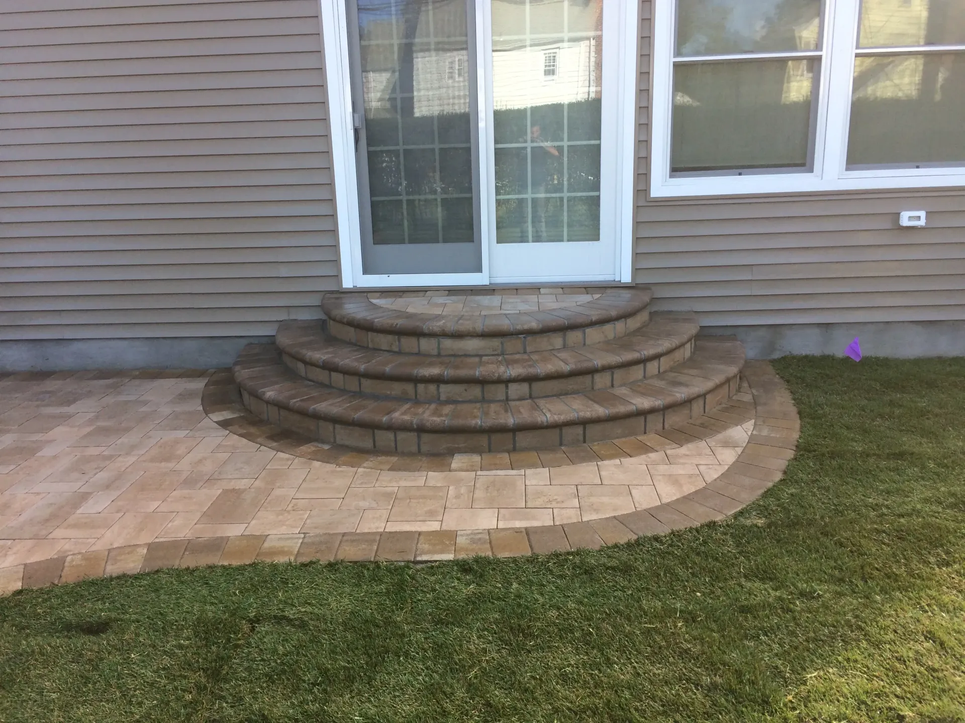 Brick steps and patio lead to sliding glass door. Green grass surrounds the stonework.