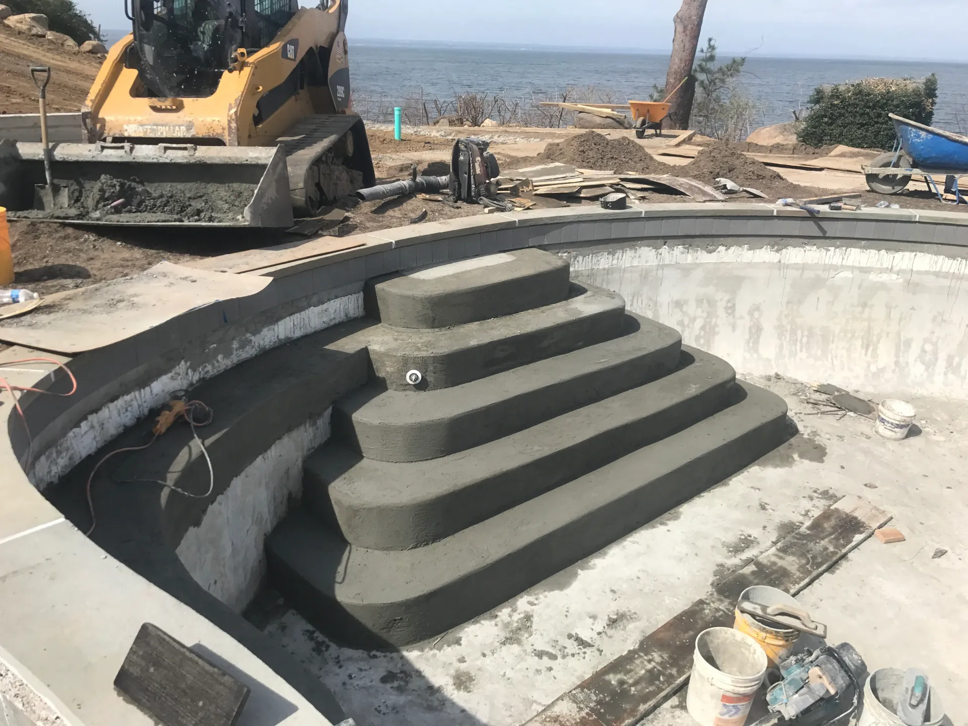 Construction of concrete steps inside a pool; a yellow skid steer in the background.