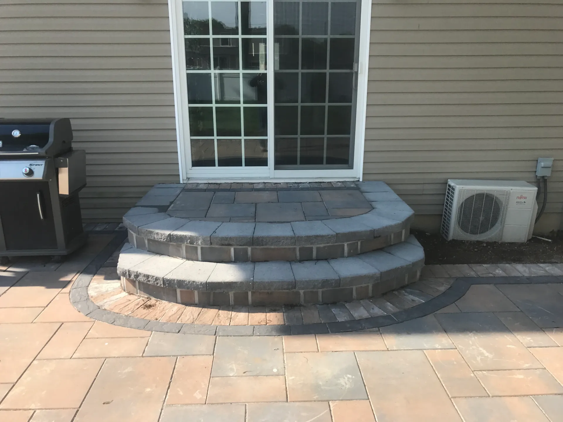 Stone steps lead up to a sliding glass door, flanked by a grill and an air conditioning unit.