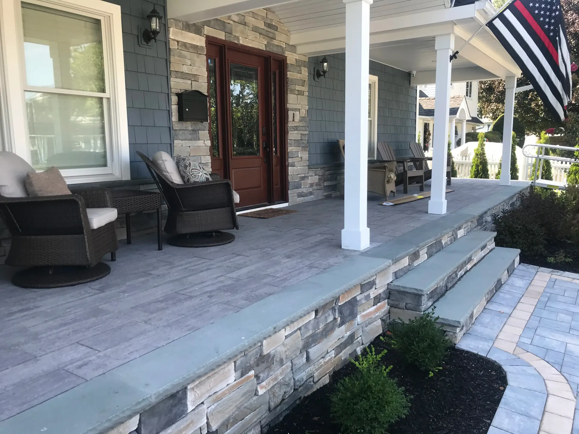 Blue house with porch, stone facade, seating, and flag.