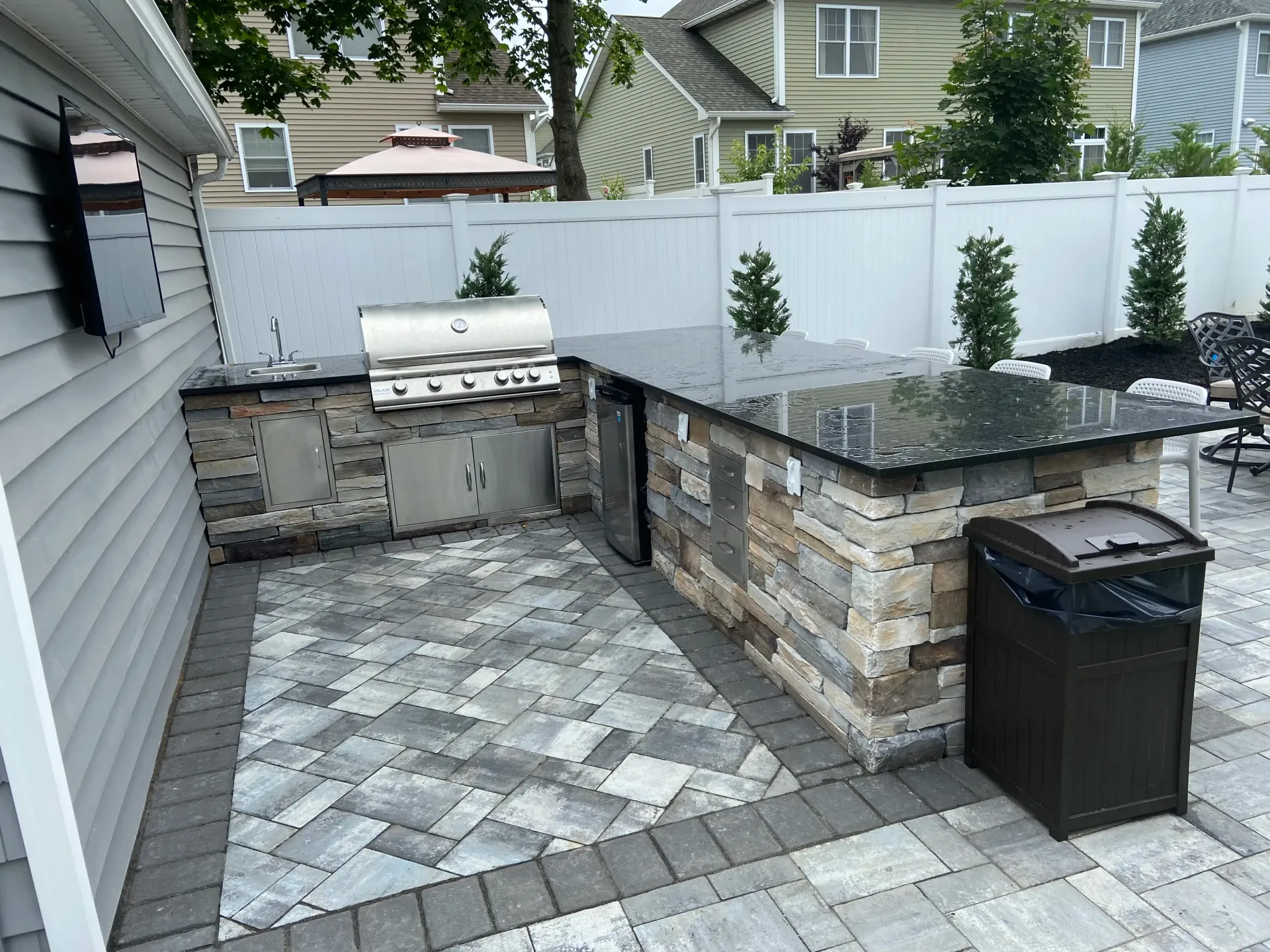 Outdoor kitchen with brickwork, stainless steel grill, and dark countertop on a stone patio.