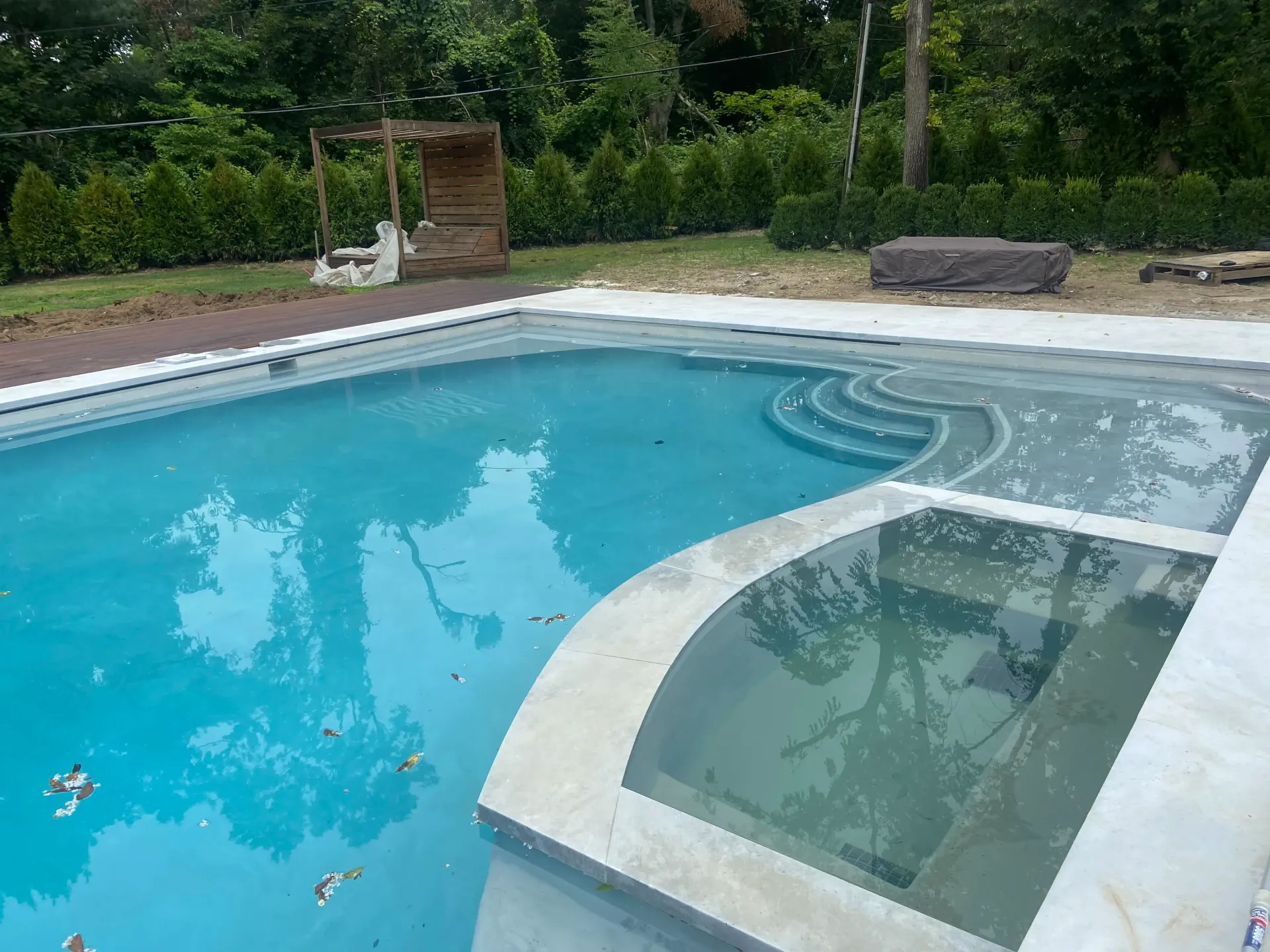 Swimming pool with attached spa; turquoise water, concrete steps, trees in the background.