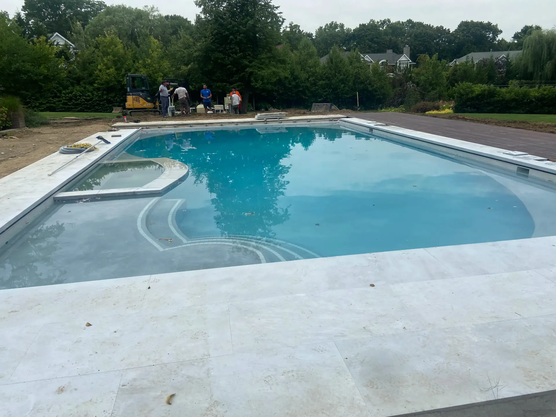 Pool construction site with workers, concrete, and turquoise water reflecting the sky.