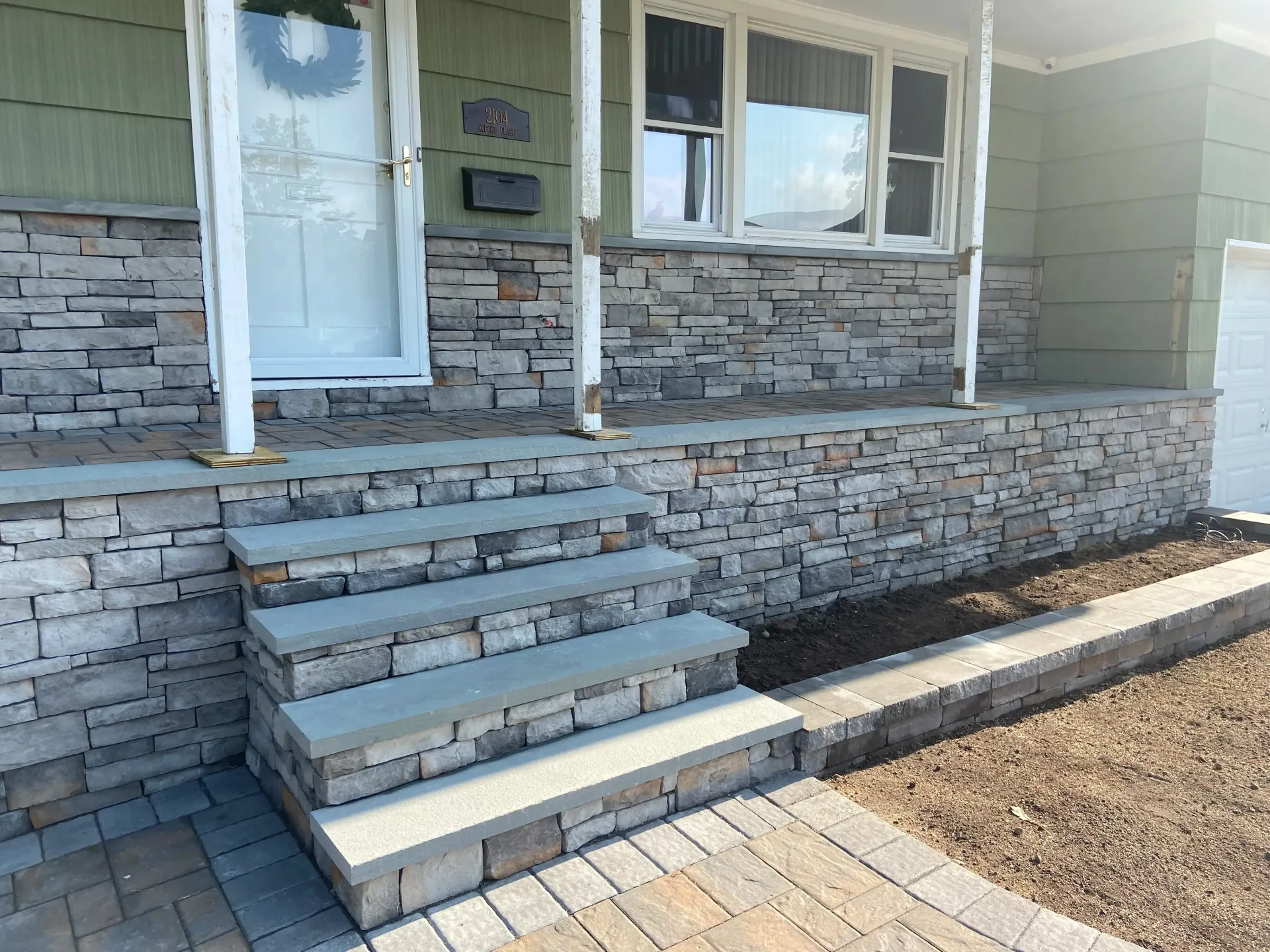 Stone steps and porch of a house with a stone facade and a paved walkway.