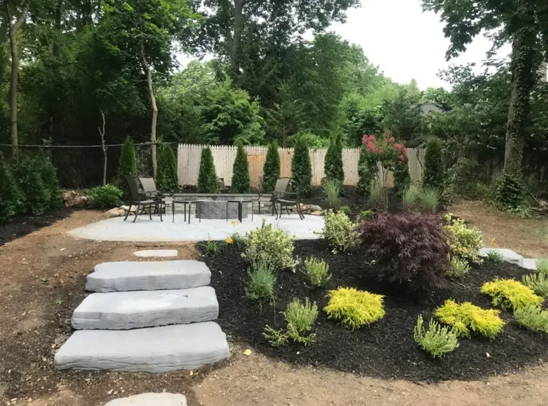 A landscape design with a stone walkway leading to a patio and a fire pit.