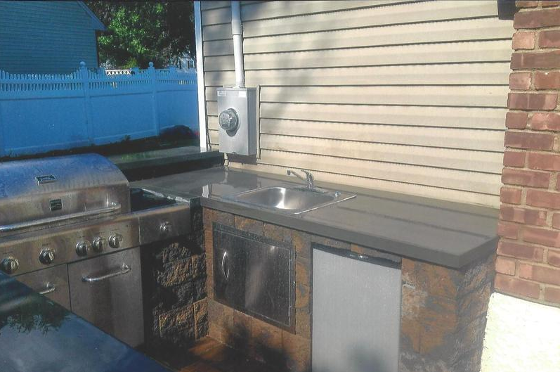 Outdoor kitchen with a grill, sink, and refrigerator, built with stone and stainless steel.