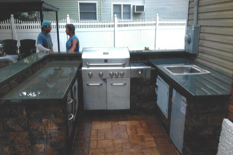 Outdoor kitchen with grill, sink, and countertop, with two people standing nearby.