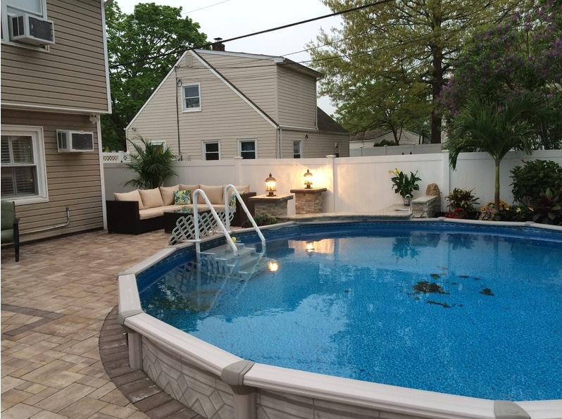 Backyard with an above-ground pool, patio furniture, and white fence. Houses in the background.