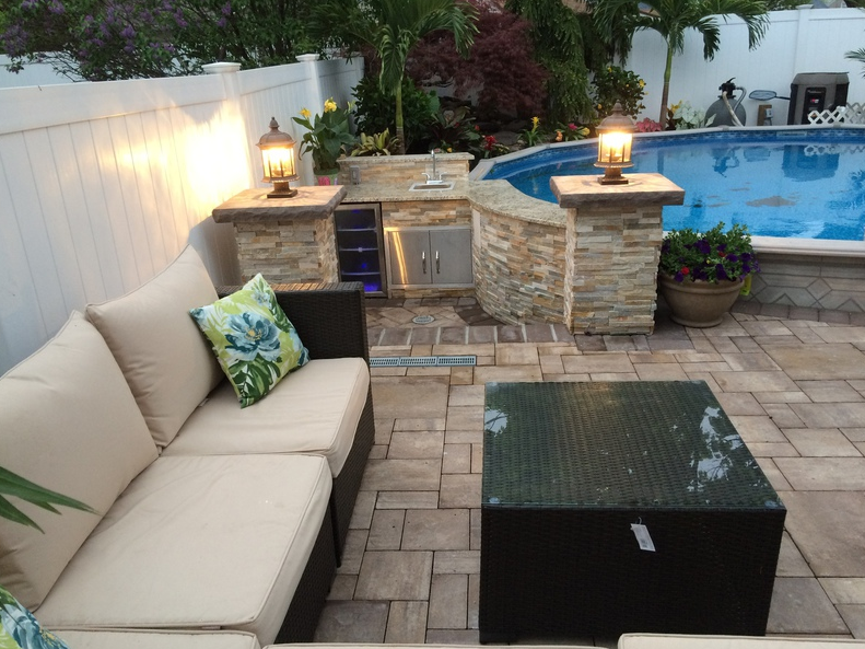Outdoor patio with couch, pool, kitchen area, and lights.
