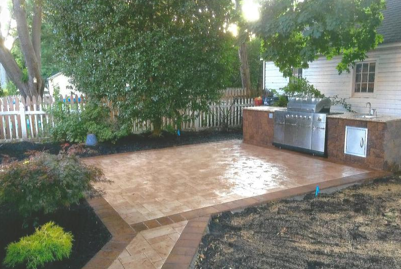 Brick patio with outdoor kitchen, stainless steel grill, and black mulch landscaping.