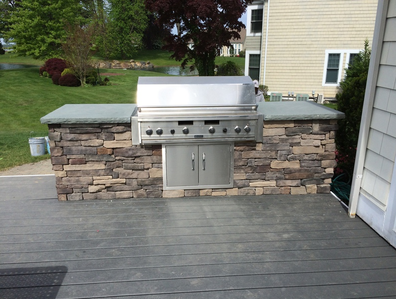 Built-in outdoor grill with stone facade on a deck; stainless steel grill and doors.