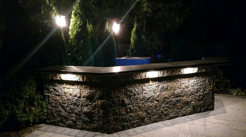 Stone outdoor bar illuminated at night with overhead lights.