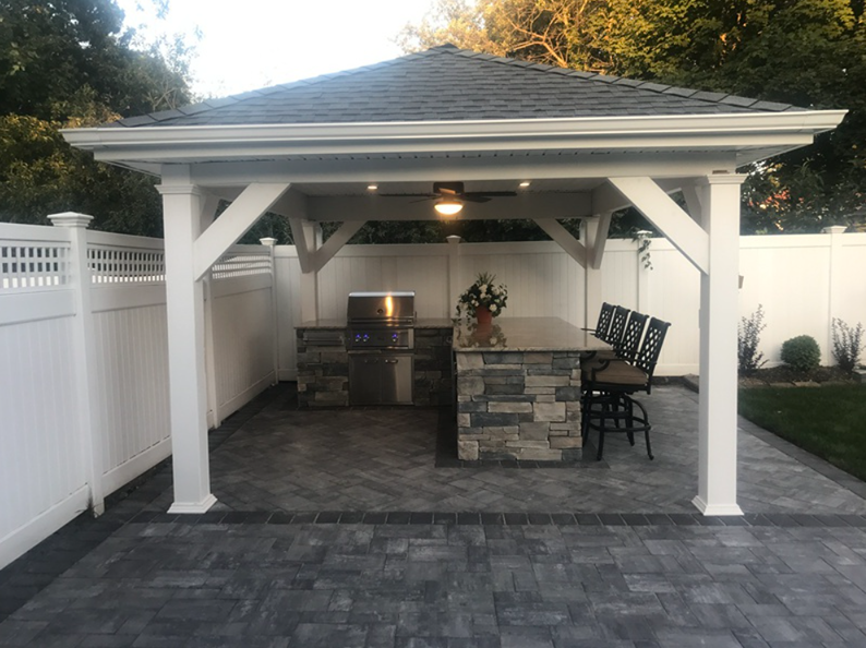Outdoor kitchen with grill, bar, and seating under a white gazebo with a stone facade.