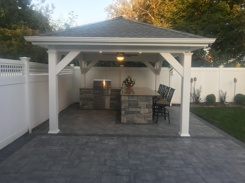 Outdoor kitchen under a white gazebo, featuring a grill and bar seating area, set on a paved patio.