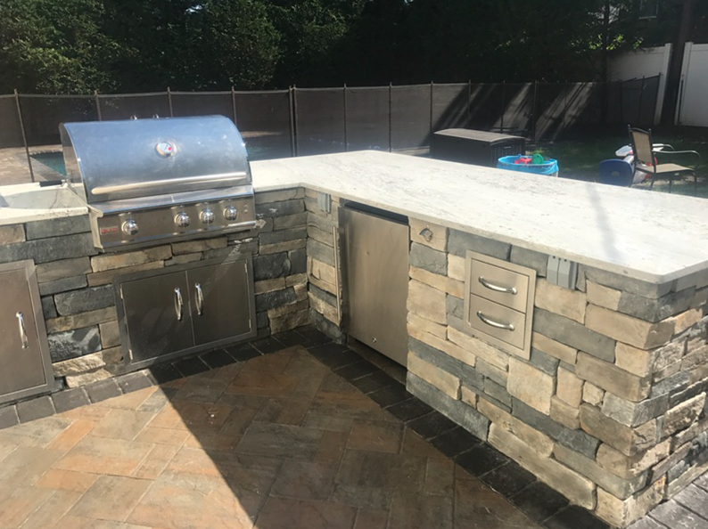 Outdoor kitchen with stainless steel grill, stone facade, and marble countertop.