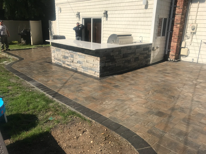 Backyard patio with an outdoor kitchen, stone pavers, and a green lawn.