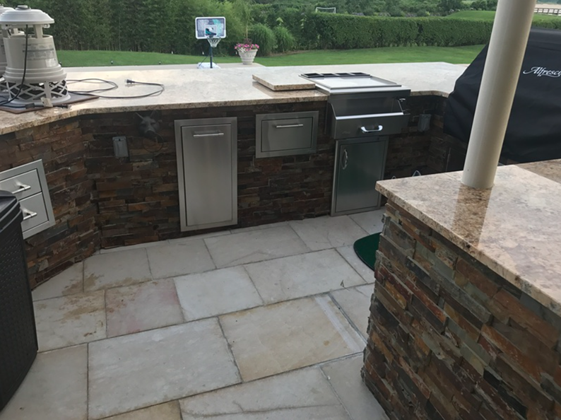 Outdoor kitchen with granite countertops, stainless steel appliances, and stone facade.