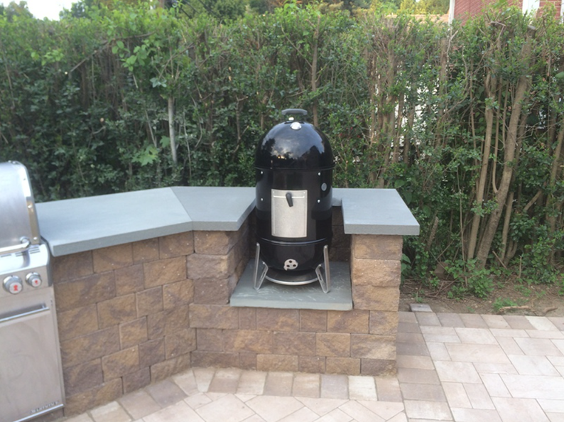 Smoker built into a brick outdoor kitchen with stone countertop.