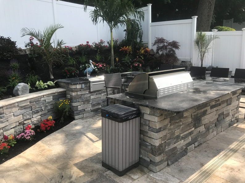 Outdoor kitchen with stone island, grill, seating, and landscaping.