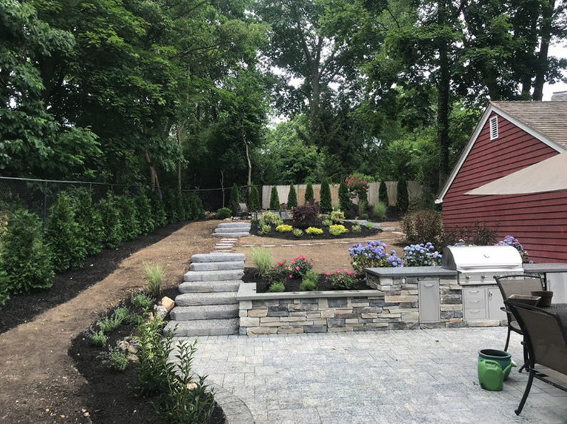 Backyard with patio, steps, garden beds, and a red house.