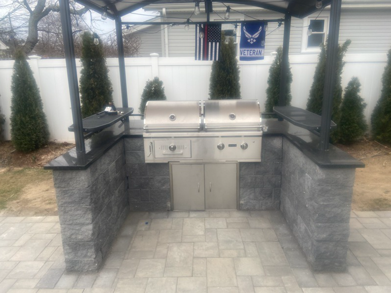 Outdoor kitchen with grill and countertops, constructed of gray brick and topped with black granite.