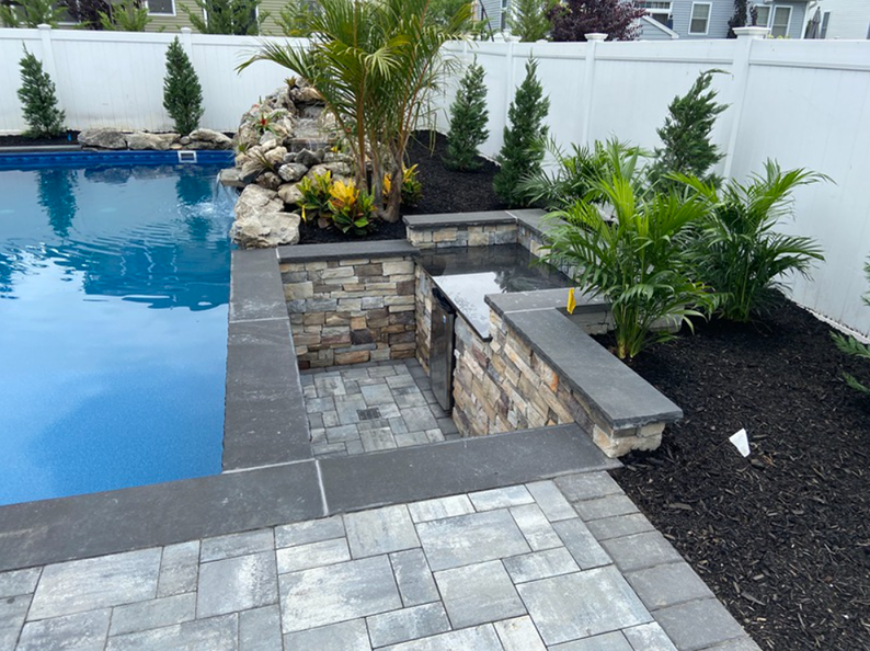 Pool with a stone patio, a small waterfall feature, and planted landscaping.