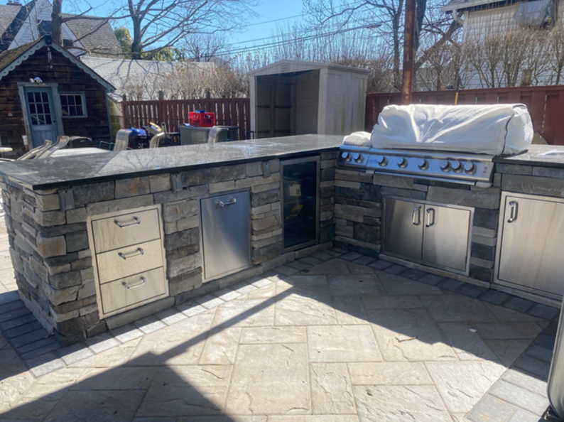 Outdoor kitchen with stone facade, granite countertop, grill, refrigerator, and storage cabinets on a patio.