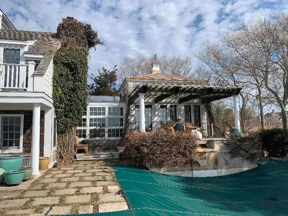 House with a pool covered in green tarp; ivy climbs the side; blue pots.