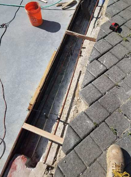 Construction of a linear drain channel, framed with wood, next to a brick-paved area.