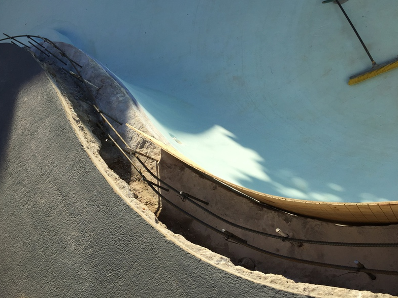 Curved concrete structure with exposed rebar; blue sky in the background.