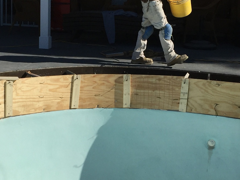 Person in work clothes near a curved wooden form around a light blue pool.
