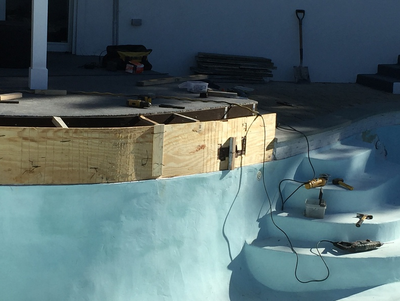 Construction of a wooden structure near a blue pool, with tools and materials scattered around.