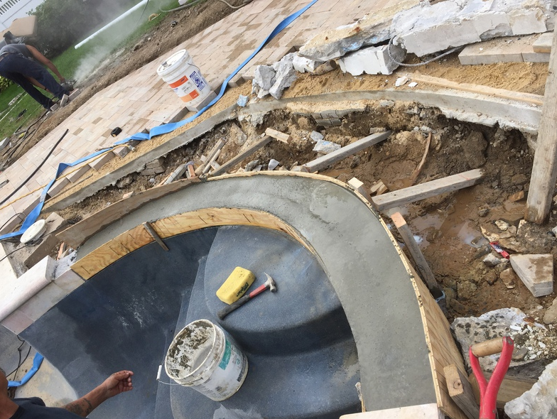 Pool renovation: Workers rebuilding pool edge with cement. Tools and debris scattered.