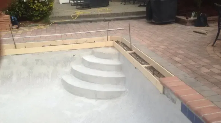 Pool under construction with steps and coping, surrounded by patio stones.