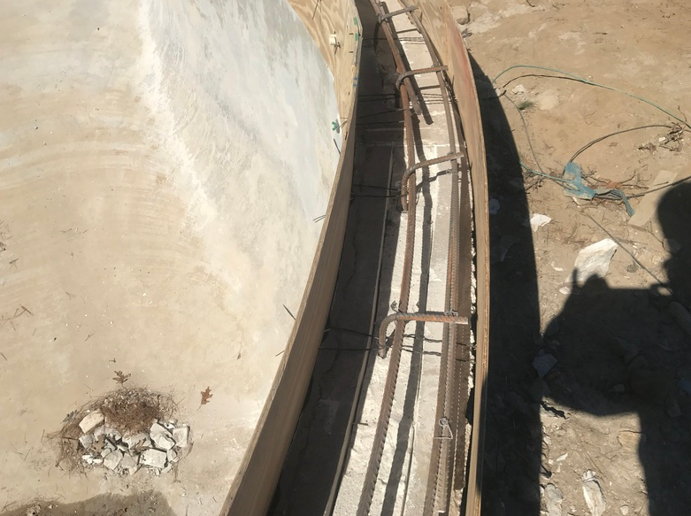 Construction site with curved concrete wall and exposed rebar framework.