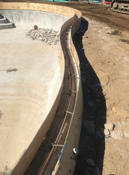 Construction of a curved concrete structure, with rebar inside wooden forms and soil surrounding.