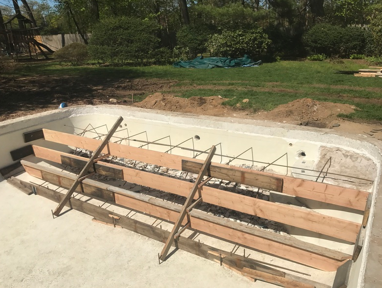 Pool construction: Wooden forms and rebar framework for steps being built in a concrete pool. Outdoors, sunny.