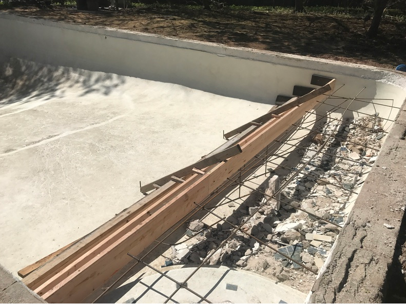 Construction site: empty pool with demolished steps and exposed rebar.