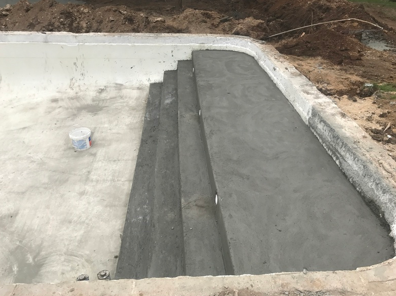 Concrete pool under construction with steps, light gray surfaces, and a white edge.