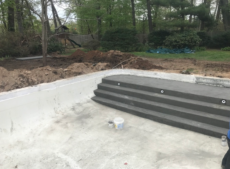 Concrete pool under construction, with gray steps and surrounding dirt in a yard.