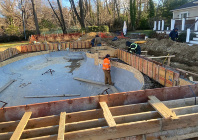 Construction site with workers building a curved pool. Wooden forms and concrete visible.