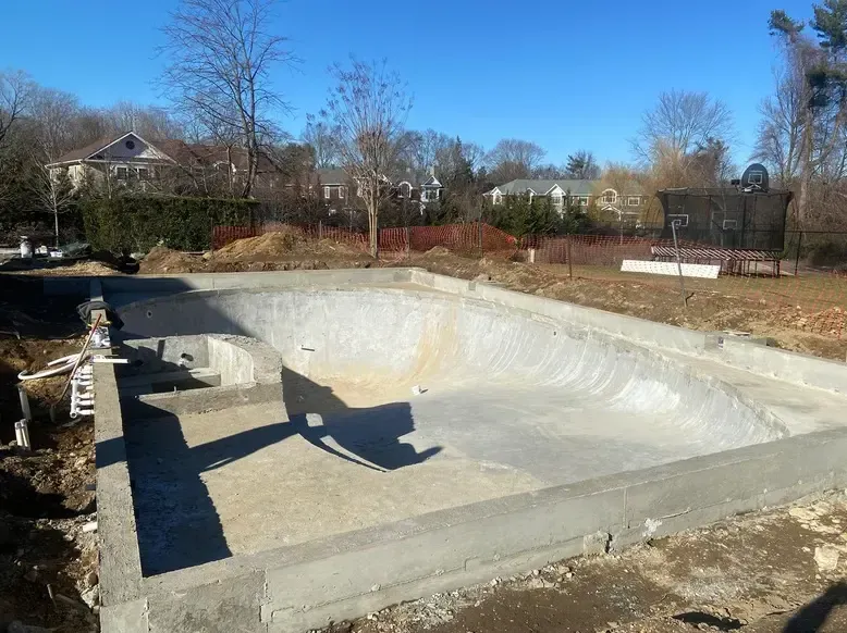 Empty concrete swimming pool under construction in a yard on a sunny day.