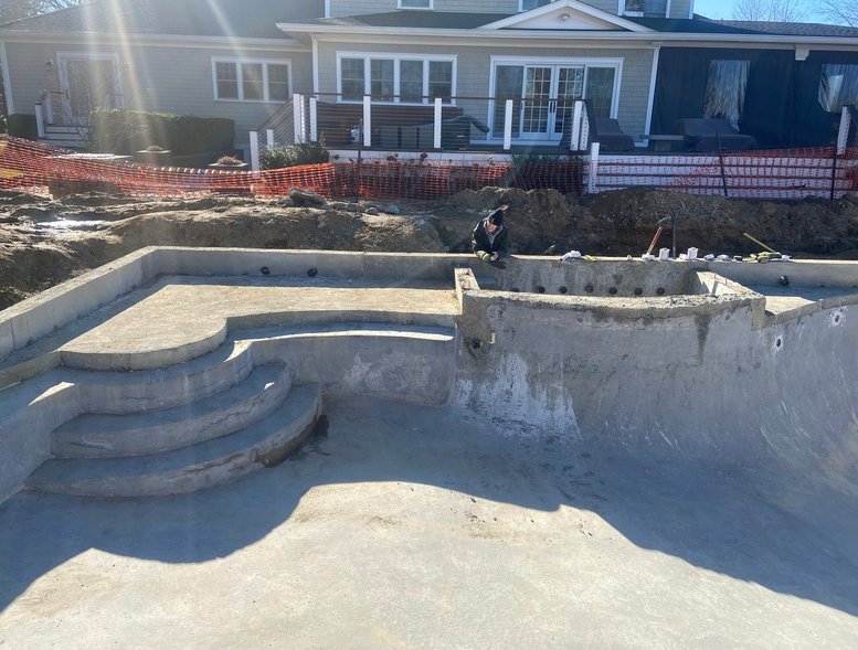 Construction of a concrete swimming pool with stairs. A person works in the background.