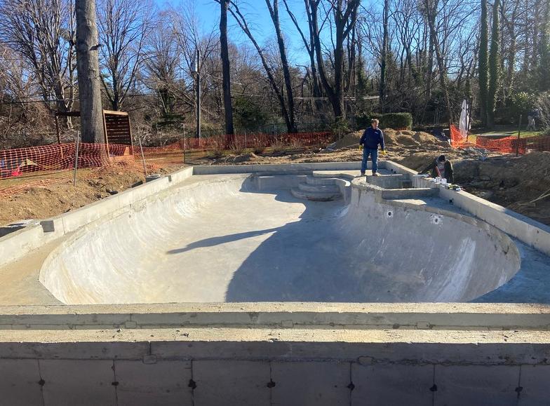 Concrete skate bowl under construction; person standing on coping. Outdoors, daytime.