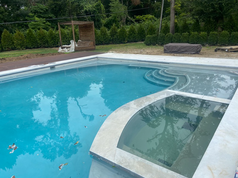 Blue pool with a built-in spa and steps, surrounded by light-colored concrete. Outdoor setting.