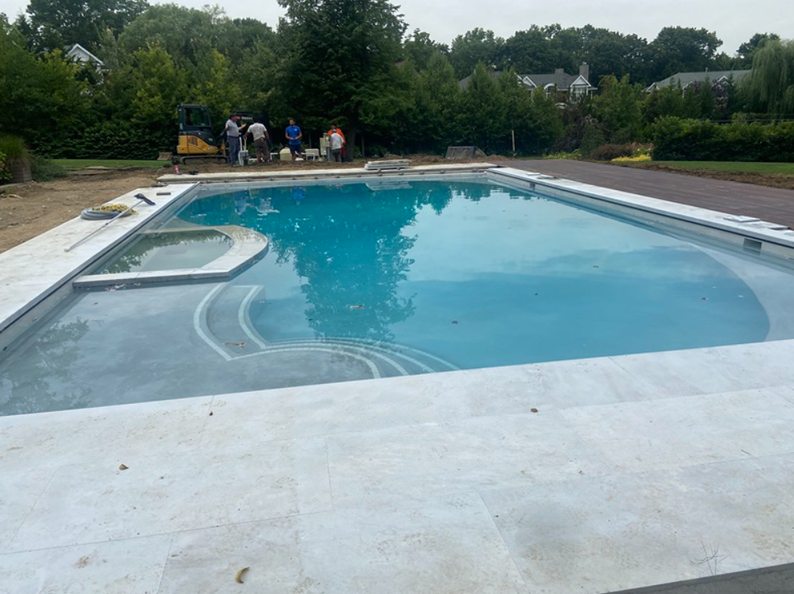 Swimming pool with a spa. Construction workers stand nearby.