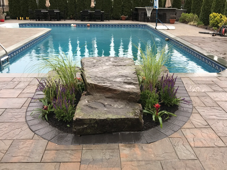 Stone steps with plants in front of a pool, set on a brick patio.