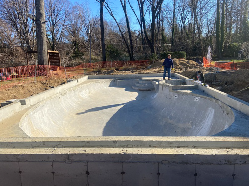 A concrete pool under construction with a person standing nearby on a sunny day.
