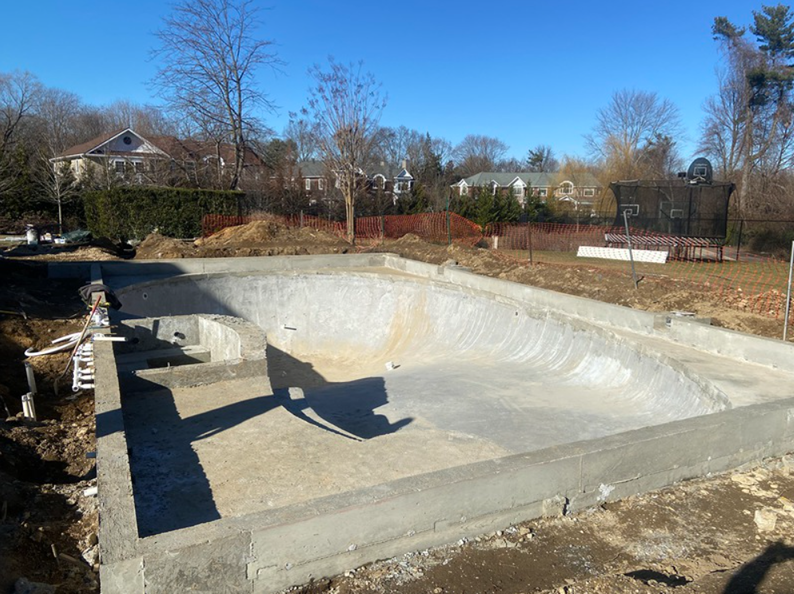 Construction site: unfinished concrete swimming pool. Houses and trees in the background on a sunny day.