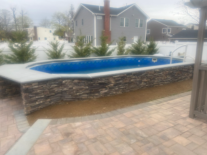 Swimming pool with stone facade in a backyard setting. Houses are in the background.
